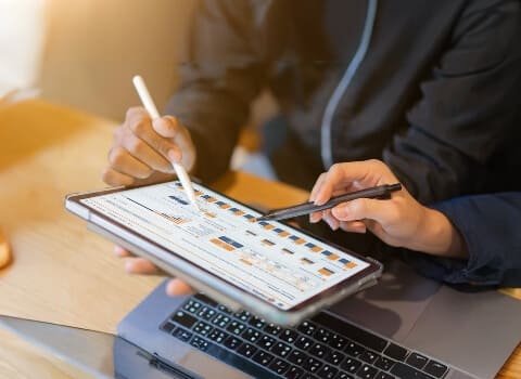 Two people reviewing cost analysis on a tablet with charts, representinghidden fees in card payment processing.