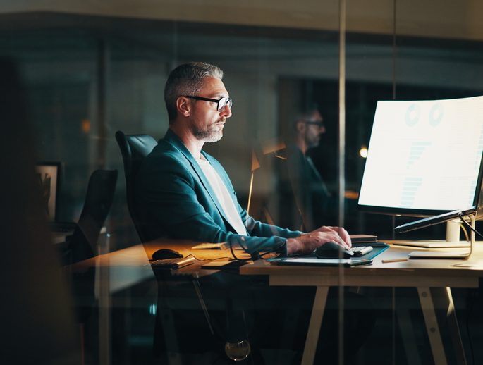 An analyst reviewing data on a monitor in an office at night